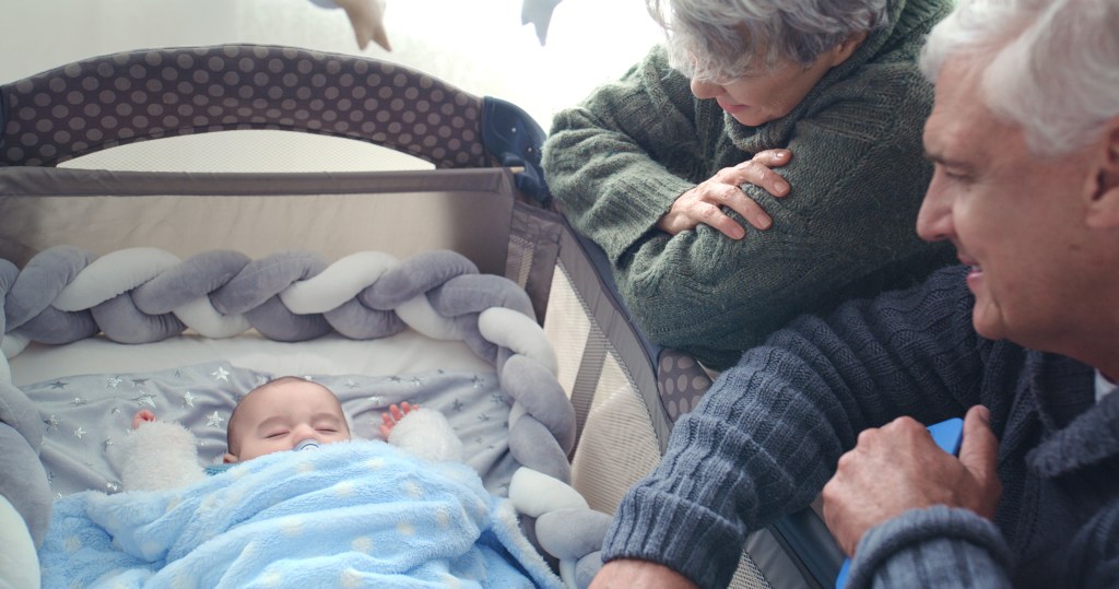 Grandparents lovingly watching their newborn grandson sleeping in a modern family nursery